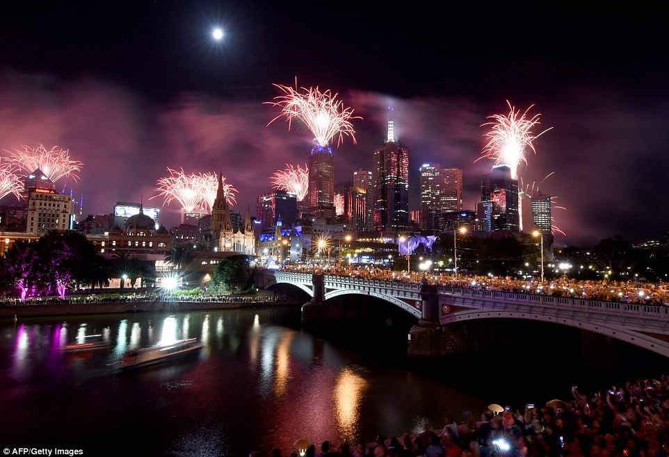 Pháo hoa nổ trên sông Yarra khi lễ kỷ niệm được tiến hành tại Melbourne, Úc. Pháo hoa sáng lên bầu trời từ những mái nhà xây dựng và hàng ngàn người tụ tập dọc theo cầu và bờ sông